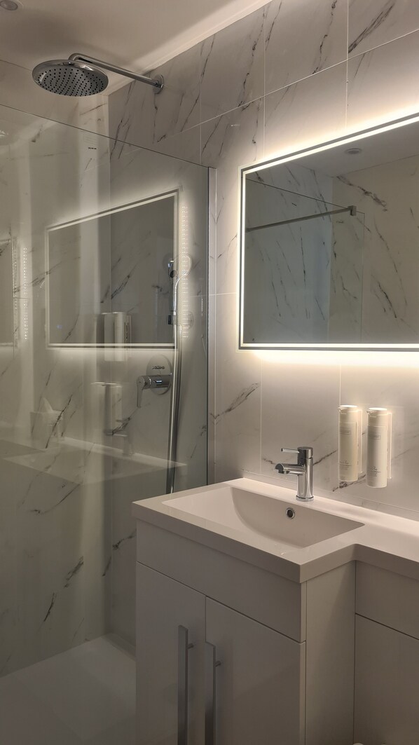 A modern bathroom with a glass-enclosed shower, a large mirror, and a vanity with a sink.