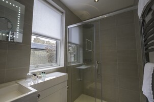 Ein modernes Badezimmer mit einer Duschkabine, einem Waschtisch mit Spiegel und einem Fenster für natürliches Licht.