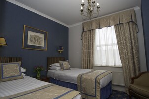 Ein Hotelzimmer mit zwei Betten, einer Kandelaber, einem gerahmten Bild an der Wand und einem Fenster mit Vorhängen.