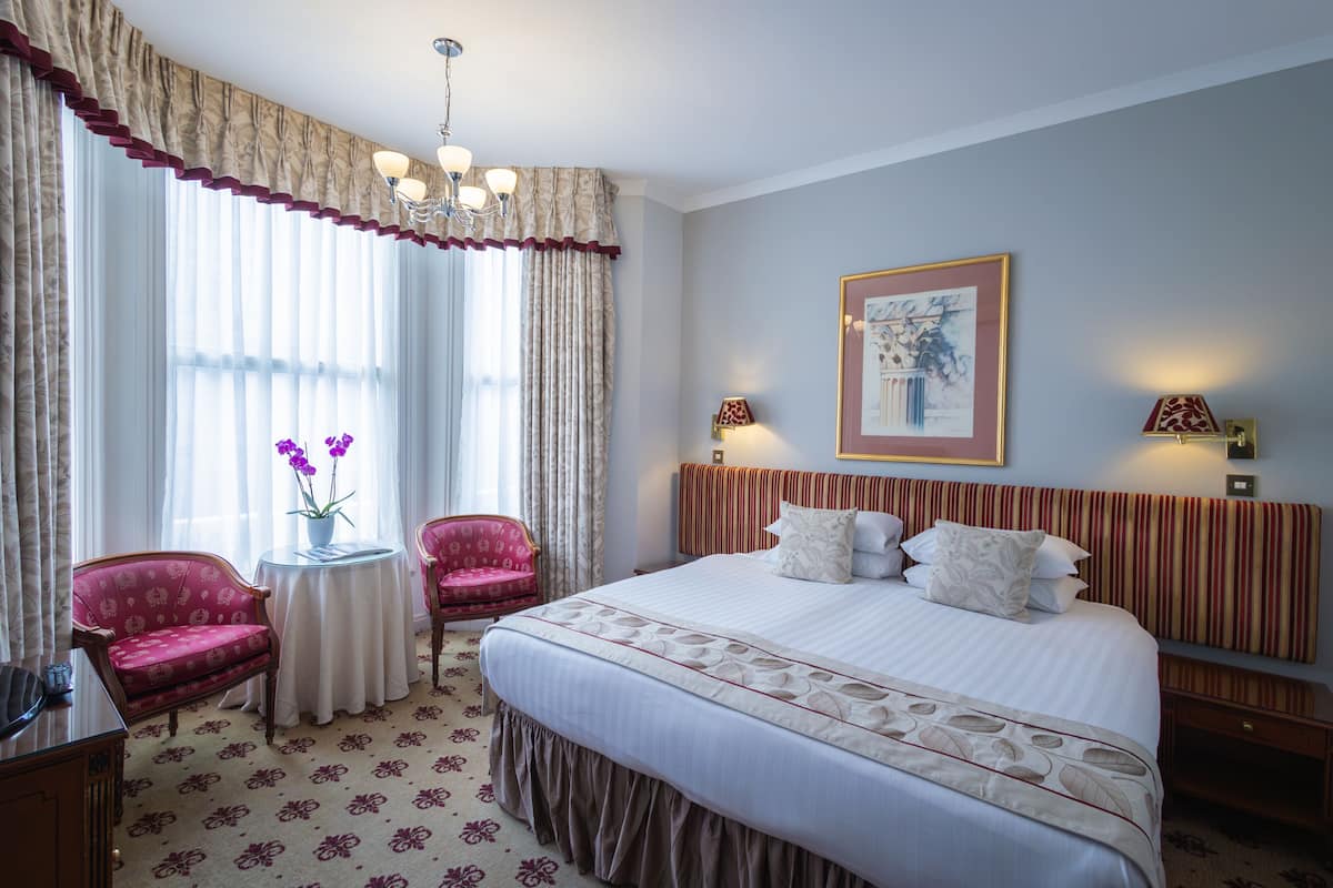 A hotel room with a large bed, two chairs, a small table, and a chandelier.