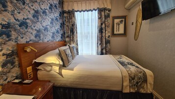 A neatly made bed with a wooden headboard, a bedside table with a lamp, and a framed picture on the wall.