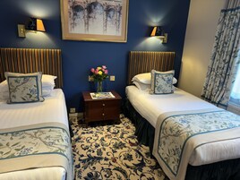 Ein Hotelzimmer mit zwei Betten, einem Nachttisch mit Blumenvase, einem gerahmten Bild an der Wand und einem gemusterten Teppich.