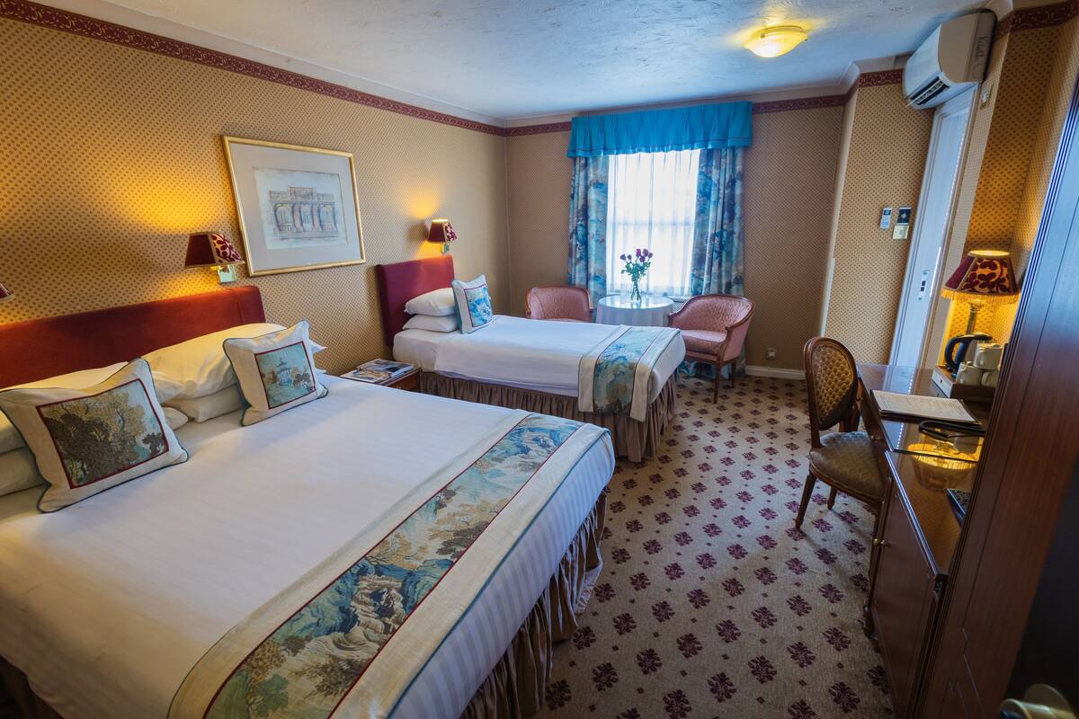 A hotel room with two beds, a desk, a chair, a small table, and a window with curtains.