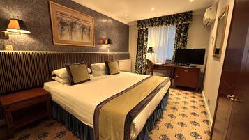 A hotel room with a large bed, a desk with a computer, a television, and a window with curtains.