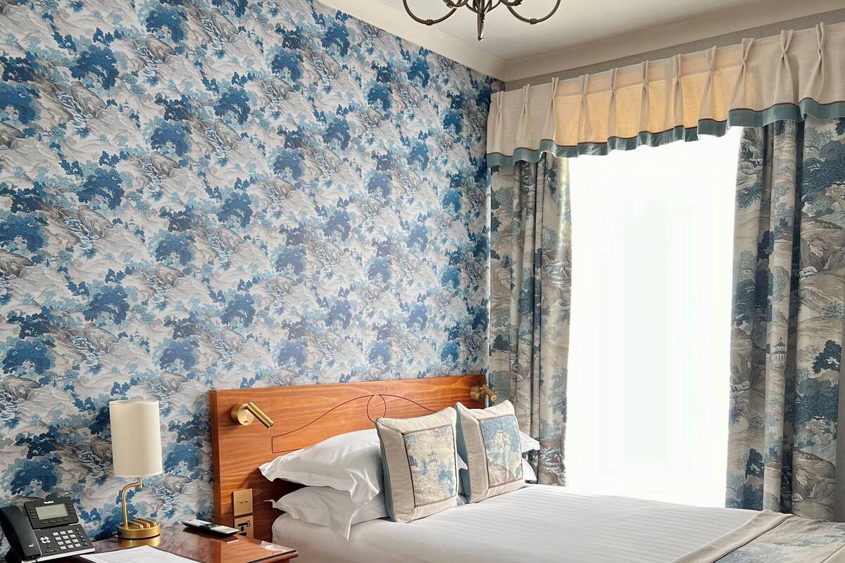 A hotel room with a bed, a desk with a telephone, a chair, a bedside table with a lamp, and a coffee maker.