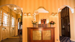 A hallway with striped wallpaper, a wooden console table with a mirror, books, and flowers, and a patterned carpet. - London Lodge Hotel (London)
