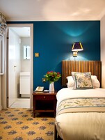 Ein Hotelzimmer mit Bett, Nachttisch, Lampe, Blumen in einer Vase und einem Telefon.