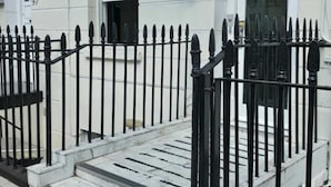 A hotel entrance with a signboard, a metal gate, and a staircase leading to the entrance.
