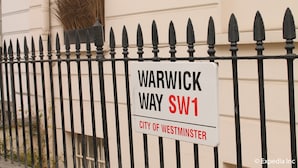 A sign on a black metal fence indicating 'Warwick Way SW1' and 'City of Westminster'.