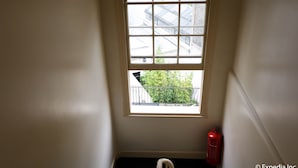 A corner of a room with a window, a fire extinguisher, and a black object on the floor.