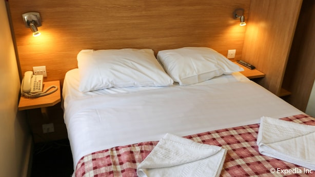 A hotel room with a wooden headboard, two bedside lamps, a telephone, and a checkered bedspread.