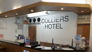 A hotel reception area with a sign reading "Colliers Hotel" and clocks displaying Tokyo, New York, and London times.