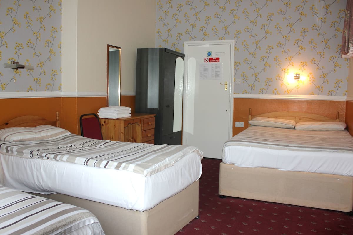 A hotel room with two beds, a wooden dresser, a mirror, and a door with a 'No Smoking' sign.