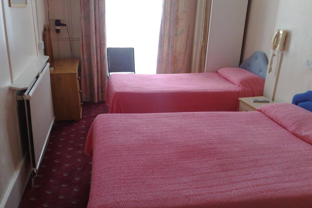 A hotel room with two beds, a desk, a chair, a radiator, and a telephone.