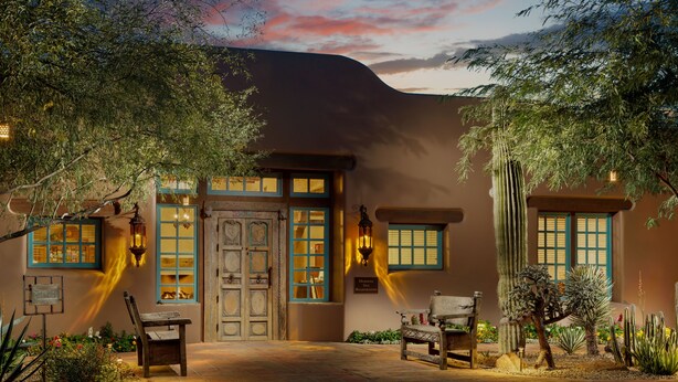 A traditional building with a large wooden door, multiple windows with blue trim, and a well-maintained garden with cacti and other desert plants. - Hermosa Inn (Paradise Valley)