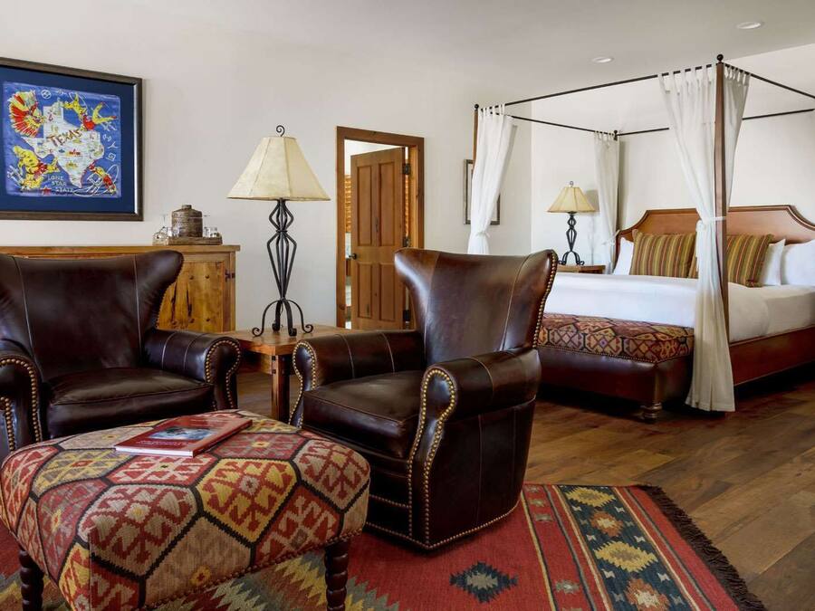 Una habitación con una cama con dosel, dos sillones de cuero, una mesa de madera y una alfombra colorida.
