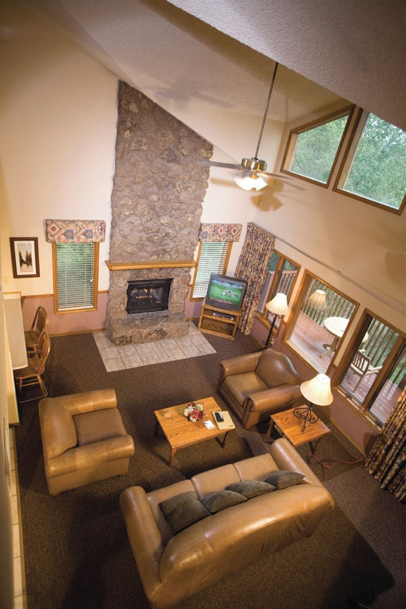 A living room with a stone fireplace, leather sofas, a television, and a ceiling fan.