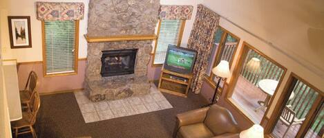 A living room with a stone fireplace, leather sofas, a television, and a ceiling fan.