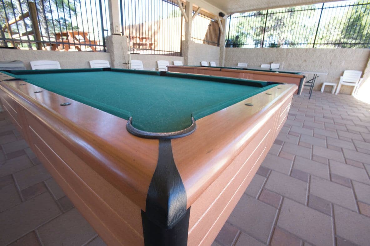 A pool table with a green felt surface, surrounded by chairs and a brick floor.