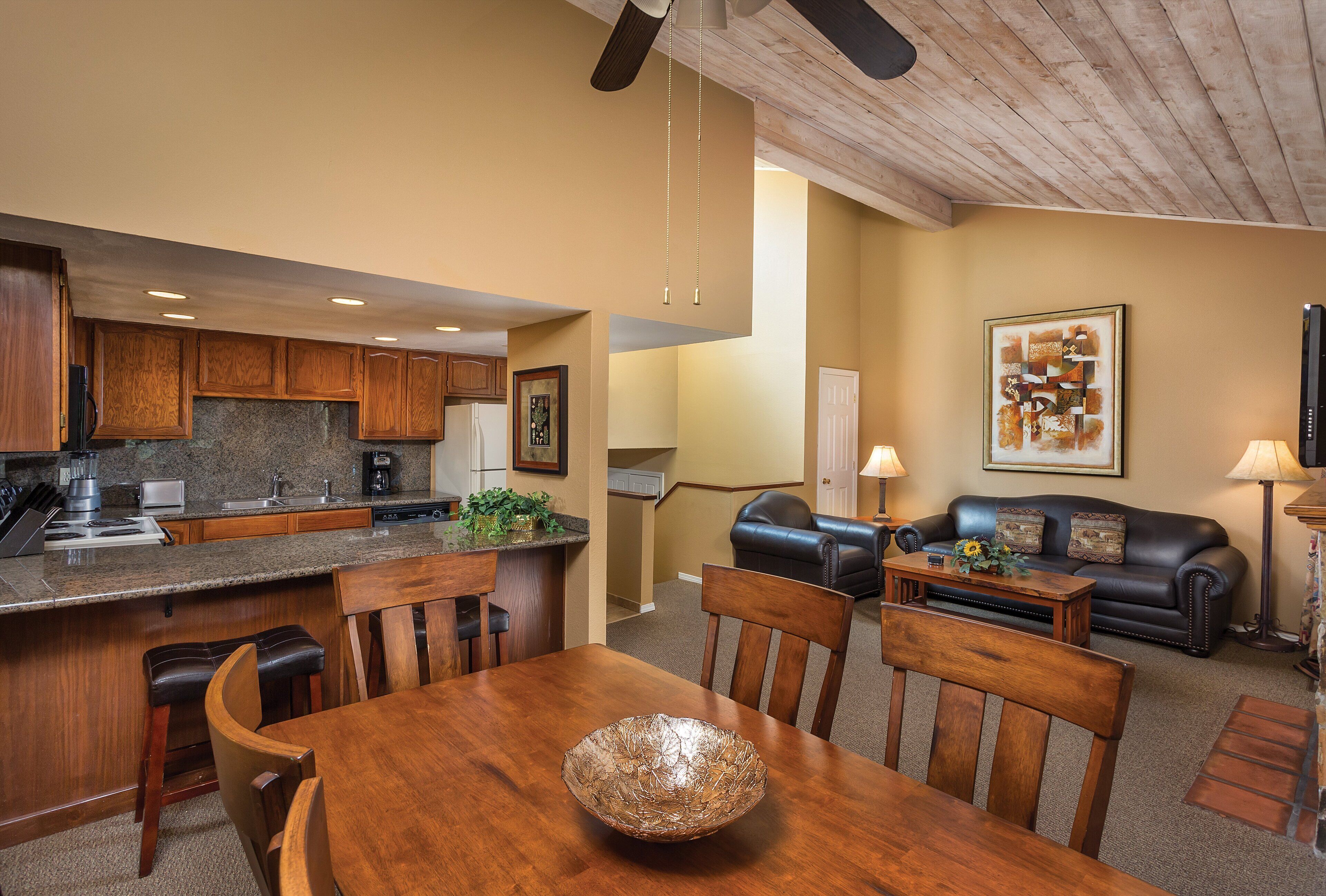Una cocina moderna con encimeras de granito, gabinetes de madera y un comedor con mesa y sillas de madera.