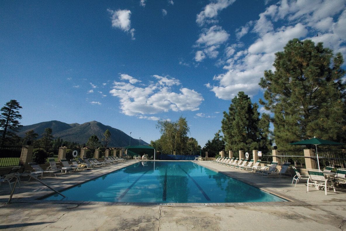 Piscina con sillas de descanso y montañas al fondo.