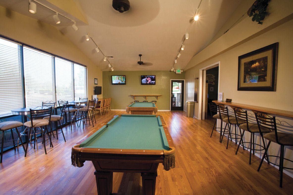 A pool table in a room with chairs and tables, a television mounted on the wall, and a door leading outside.