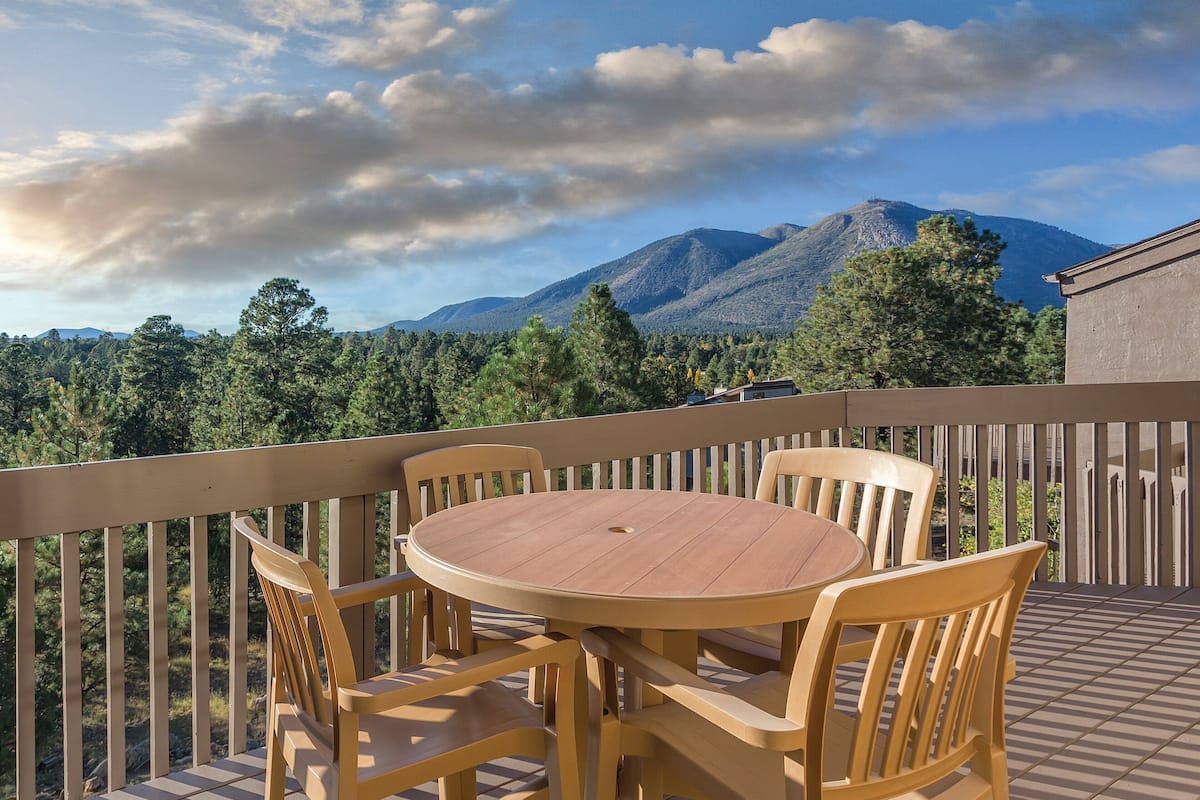 Une table et des chaises en bois sur un balcon offrant une vue sur les montagnes et les arbres.