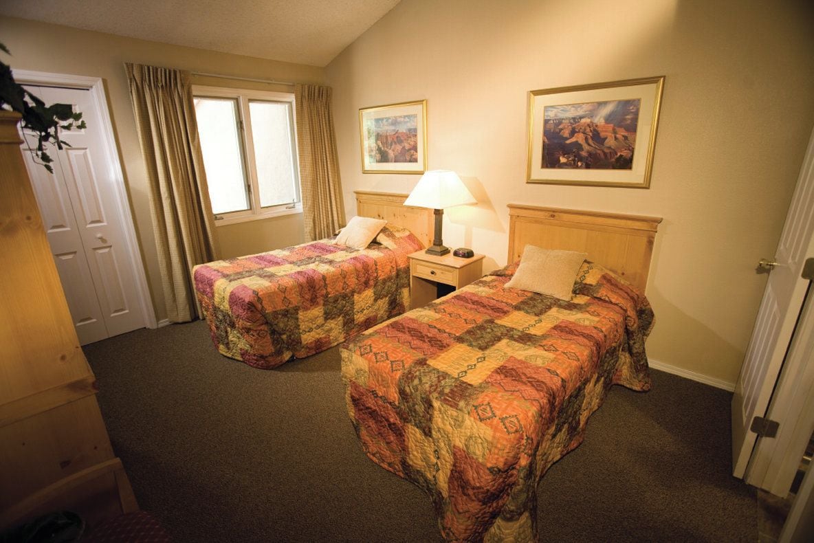 A hotel room with two beds, a nightstand, a lamp, and two framed pictures on the wall.