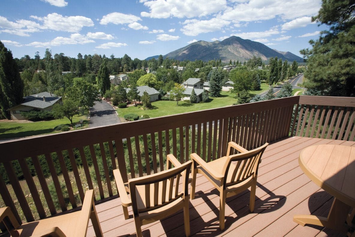 A deck with two chairs and a table, overlooking a residential area with houses and a mountain in the background.