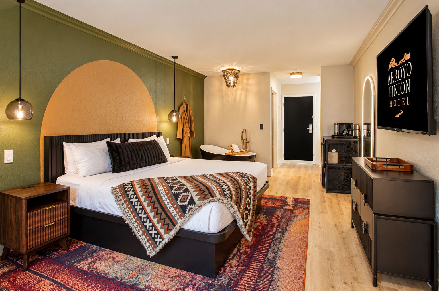 A modern hotel room with a large bed, a desk, a TV, and a wardrobe.