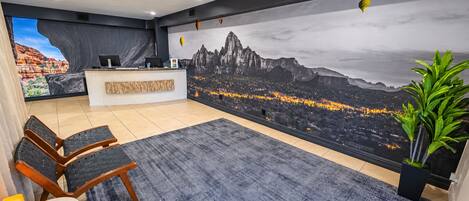 Zona de recepción de un hotel con un gran mural de la ciudad, un mostrador de recepción, un área de descanso y una planta en maceta.