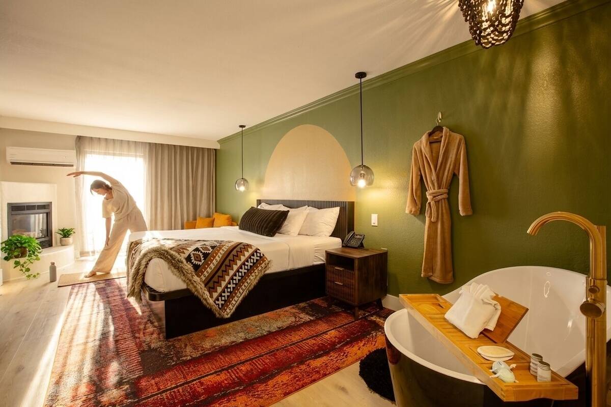 A hotel room with a bed, bedside table, robe, and a bathtub with a tray.