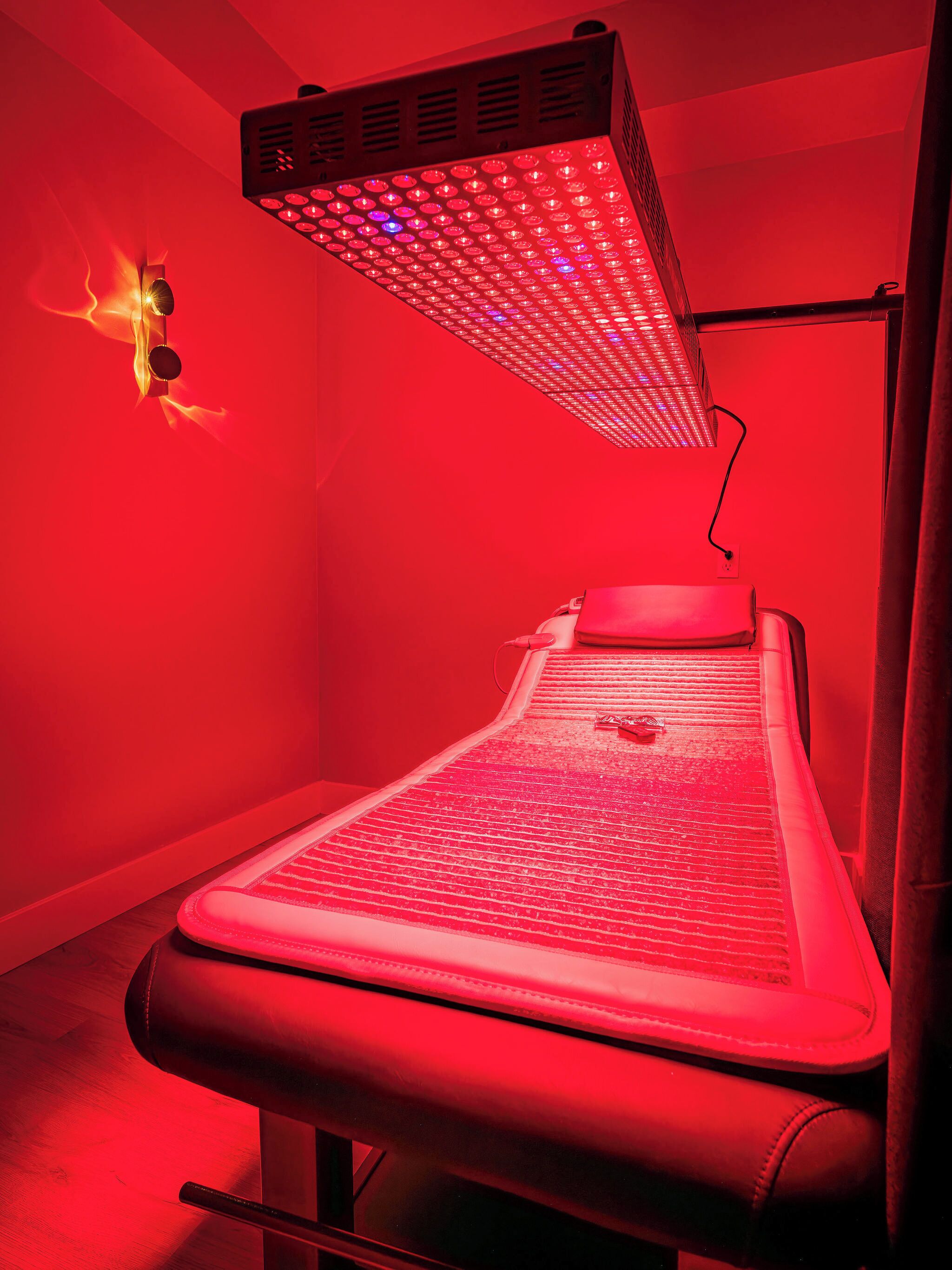 A red-lit room with a massage table, a wall-mounted heater, and a power outlet.