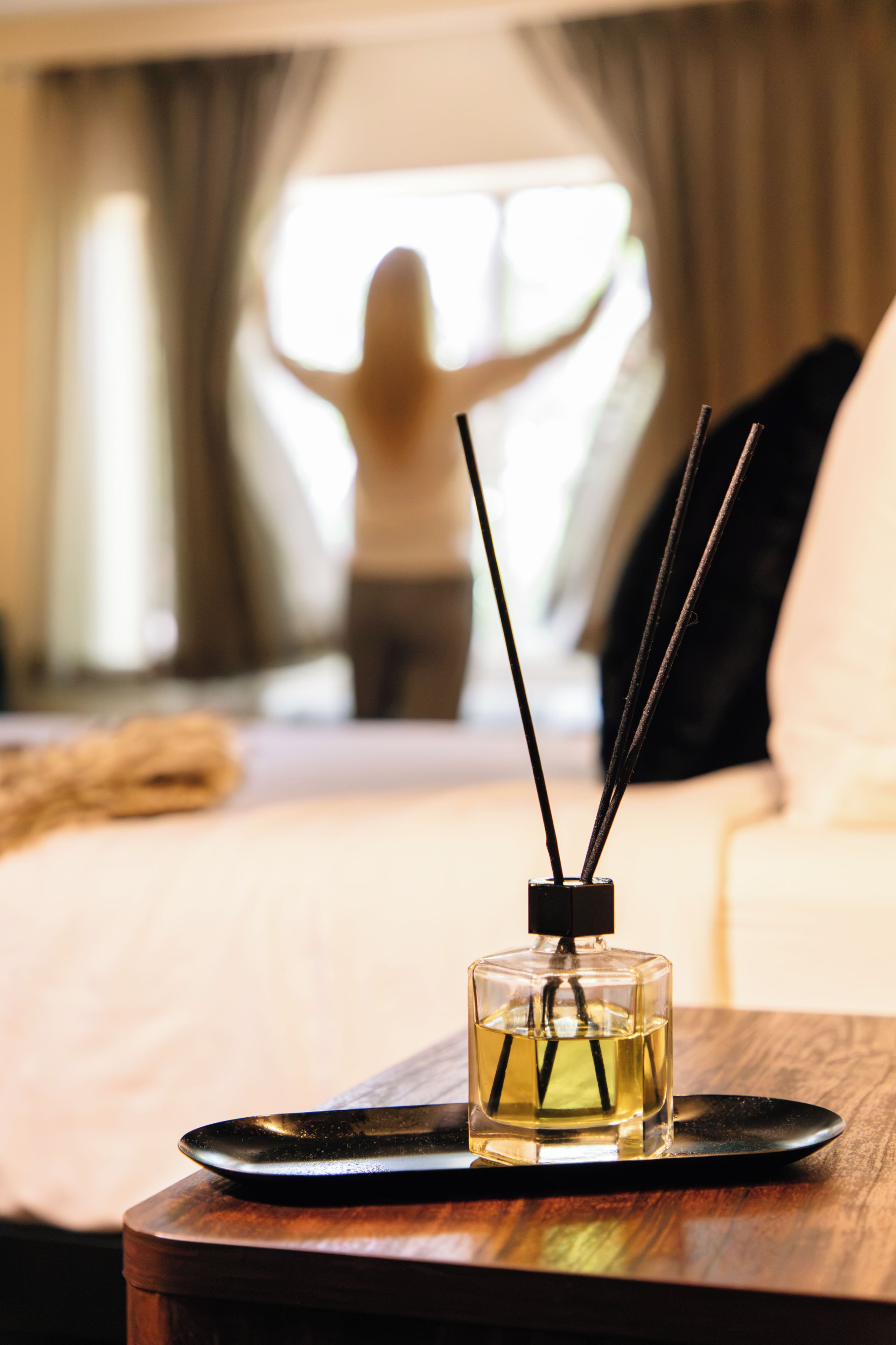 A bedside table with a glass bottle of liquid, a black tray, and a pair of black candles.