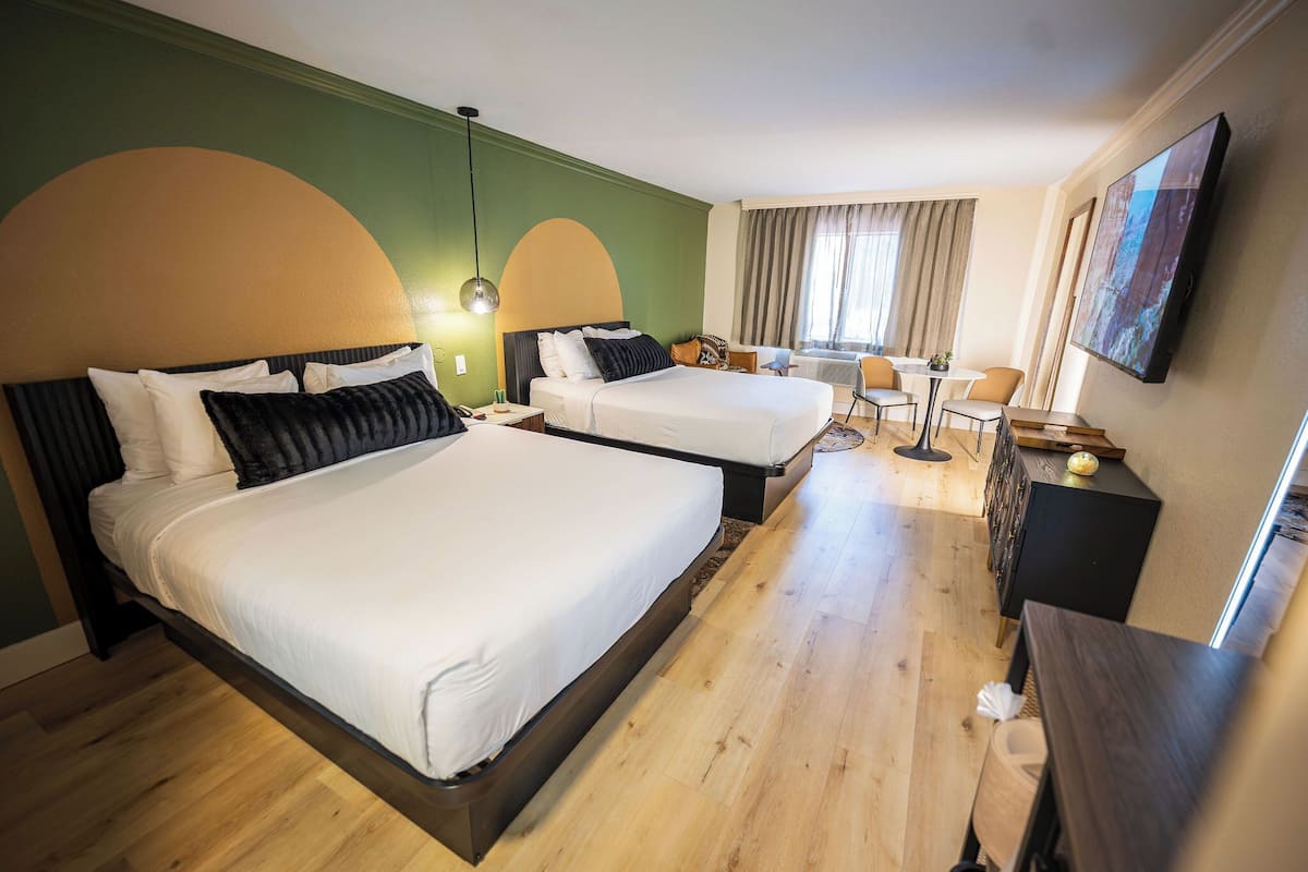 A hotel room with two beds, a desk, a chair, a television, and a window with curtains.