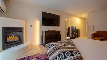 Un dormitorio moderno con chimenea, cama con ropa de cama estampada, televisor montado en la pared y espejo con luz.