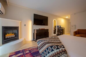 A modern bedroom with a fireplace, a bed with patterned bedding, a TV mounted on the wall, and a mirror with a light. - Arroyo Pinion Hotel, an Ascend Collection Hotel (Sedona)