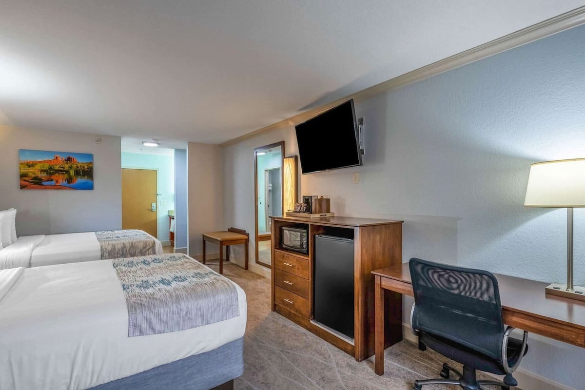 A hotel room with two beds, a desk with a computer, a TV, and a lamp.