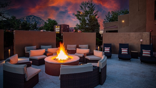 An outdoor seating area with a central fire pit surrounded by wicker furniture and cushions, set against a backdrop of a mountain and a twilight sky. - Arroyo Pinion Hotel, an Ascend Collection Hotel (Sedona)