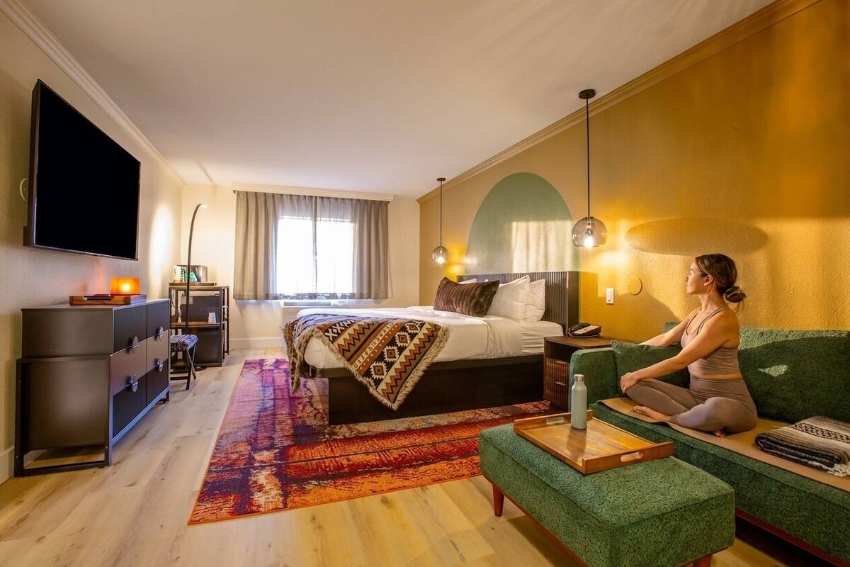 A hotel room with a bed, a green sofa, a TV, a desk, and a window with curtains.