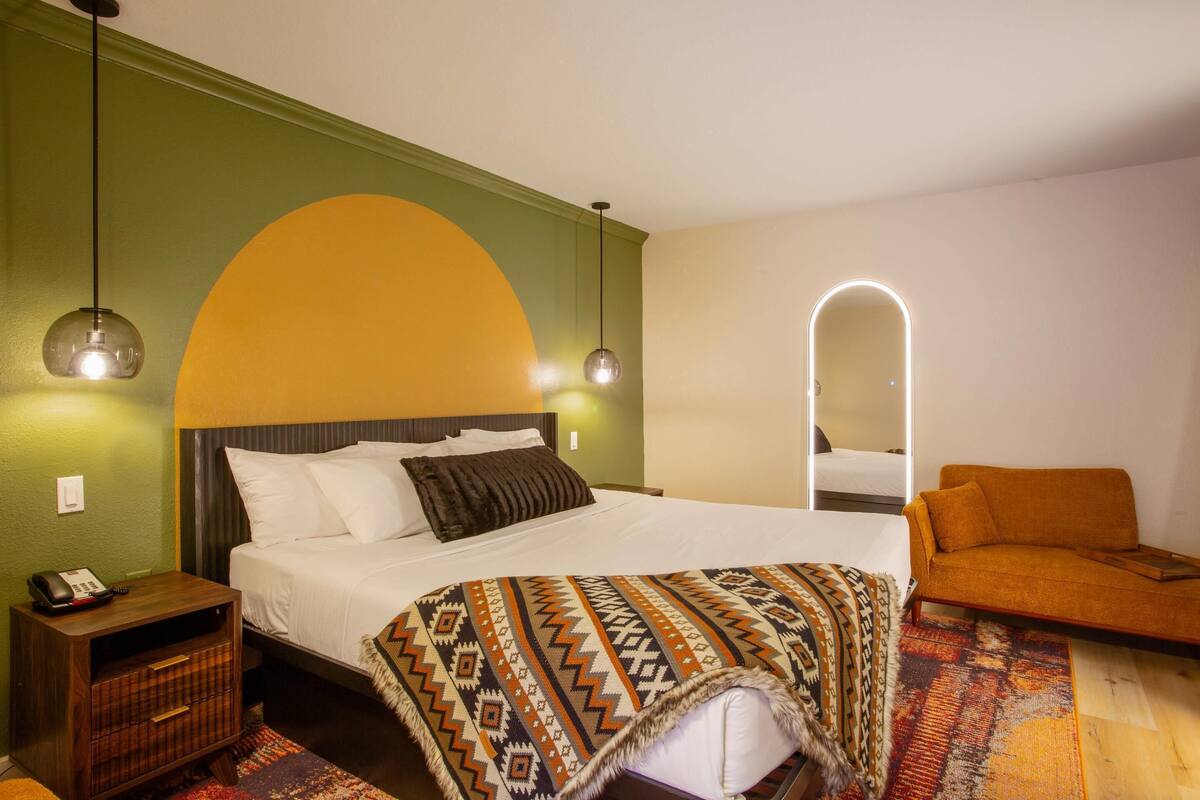 A hotel room with a bed, a nightstand, a sofa, and a mirror.