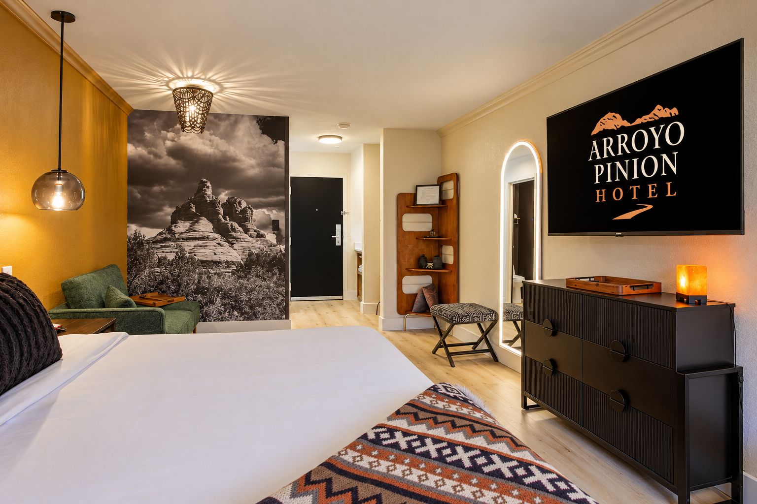 A hotel room with a bed, a desk, a chair, a dresser, a TV, and a wall with a mountain landscape.