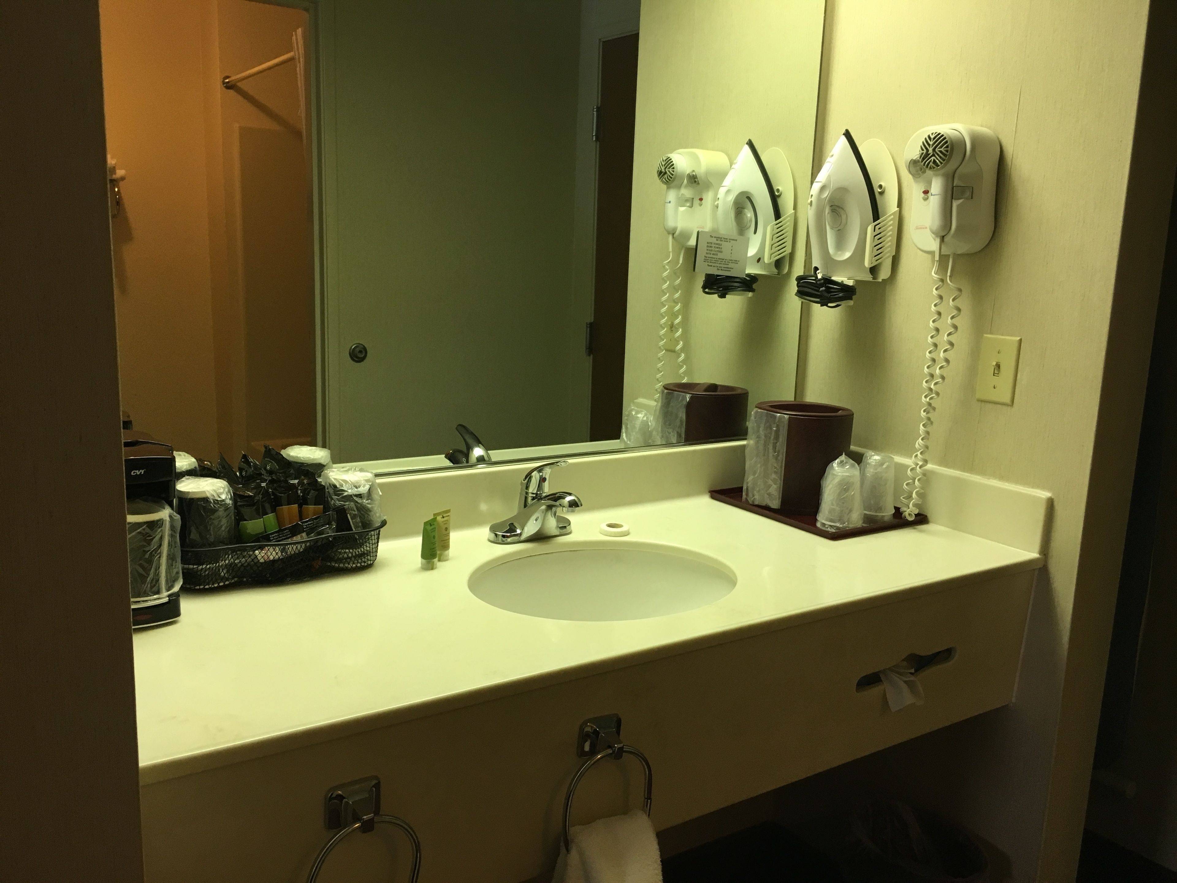 A hotel bathroom with a sink, mirror, hair dryers, and toiletries.