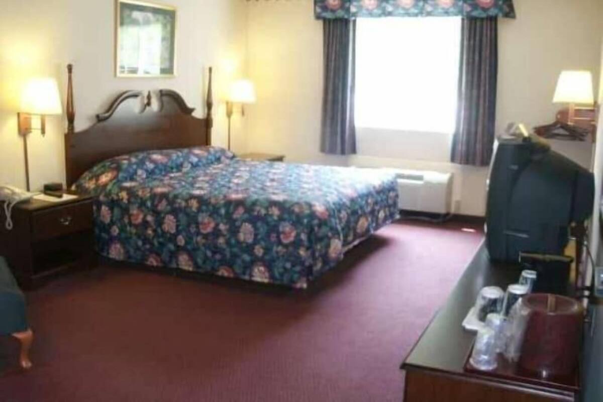 Een hotelkamer met een bed, nachtlampjes, een bureau met telefoon en een raam met gordijnen.