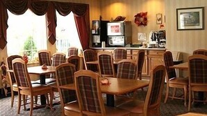 A hotel dining area with wooden tables and chairs, a television, and a coffee machine. - Baymont by Wyndham Mount Vernon Renfro Valley (Mount Vernon)