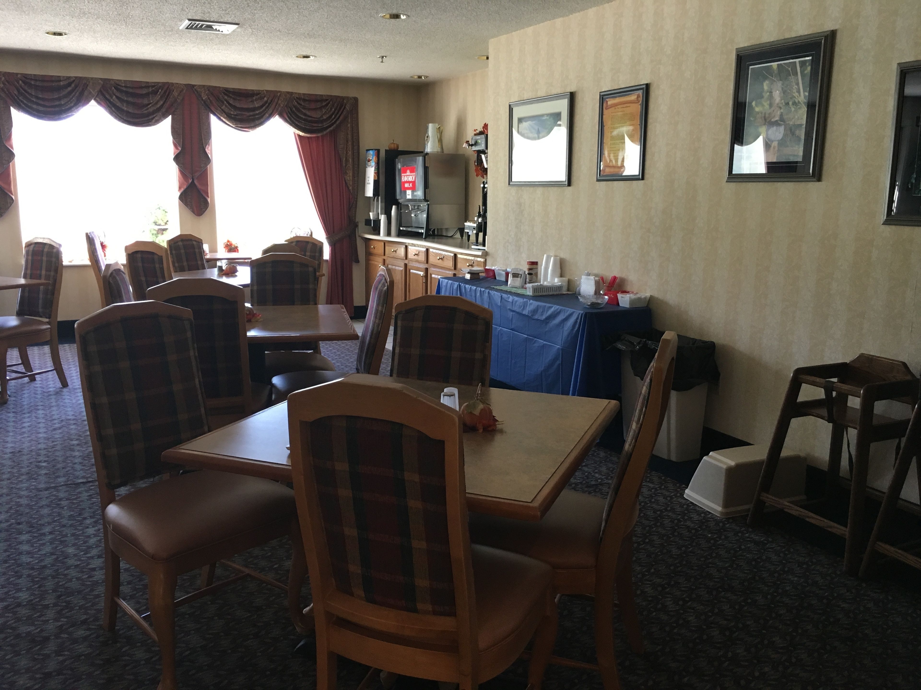 A dining area with wooden tables and chairs, a coffee station, and framed pictures on the wall.
