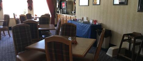 A dining area with wooden tables and chairs, a coffee station, and framed pictures on the wall.