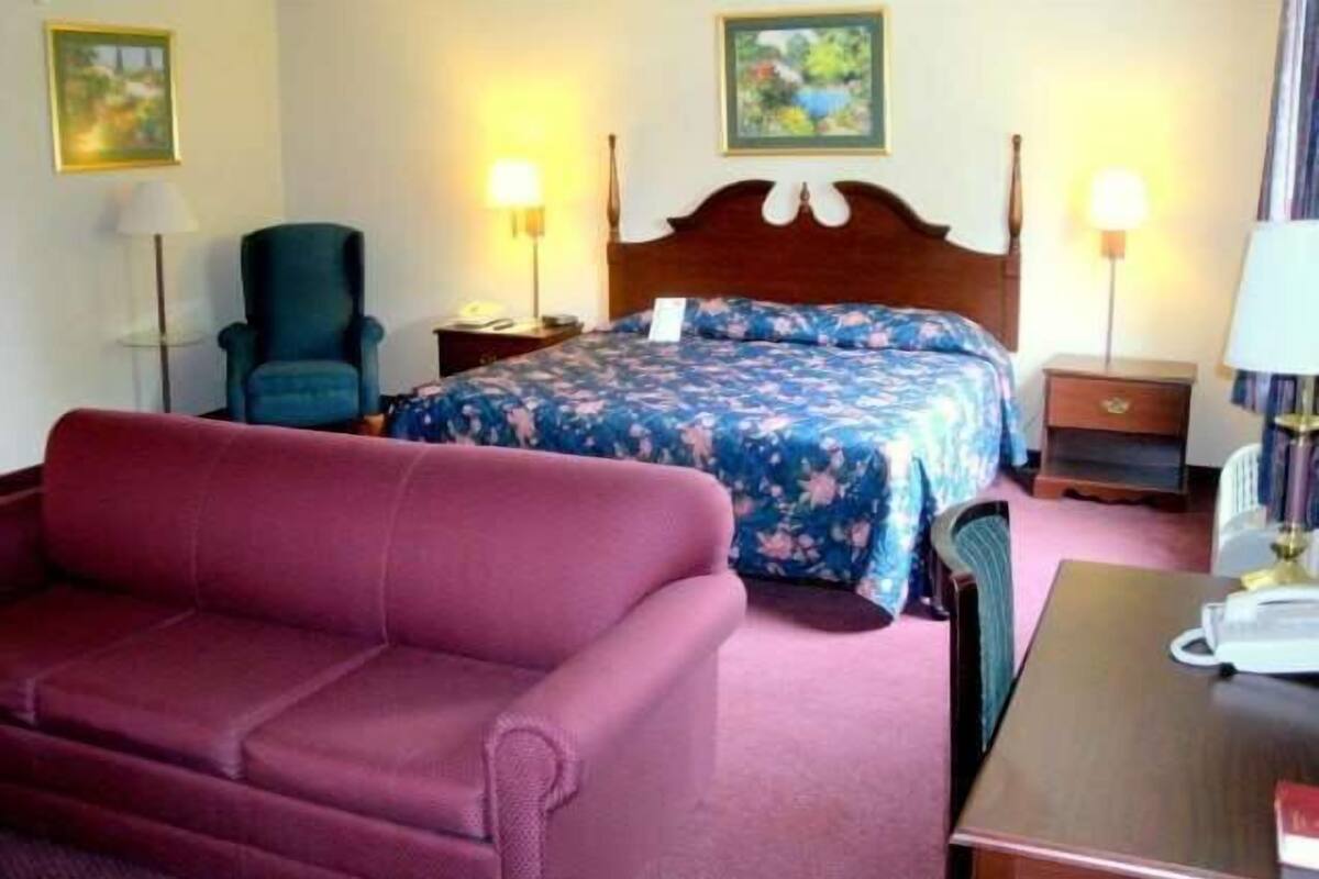 Een hotelkamer met een bed, een rode bank, een houten nachtkastje, een lamp en een stoel.