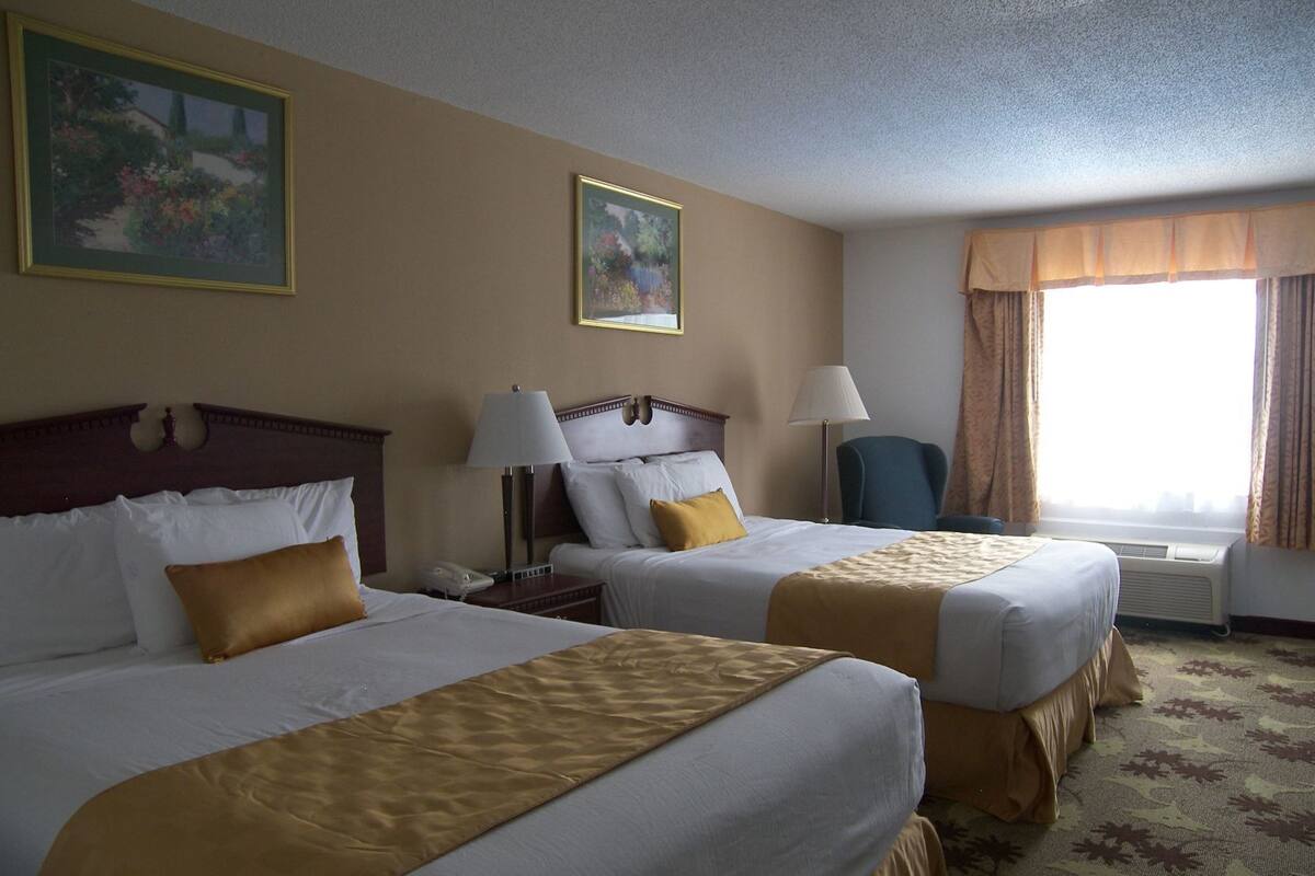 Een hotelkamer met twee bedden, een stoel, een lamp en een schilderij aan de muur.