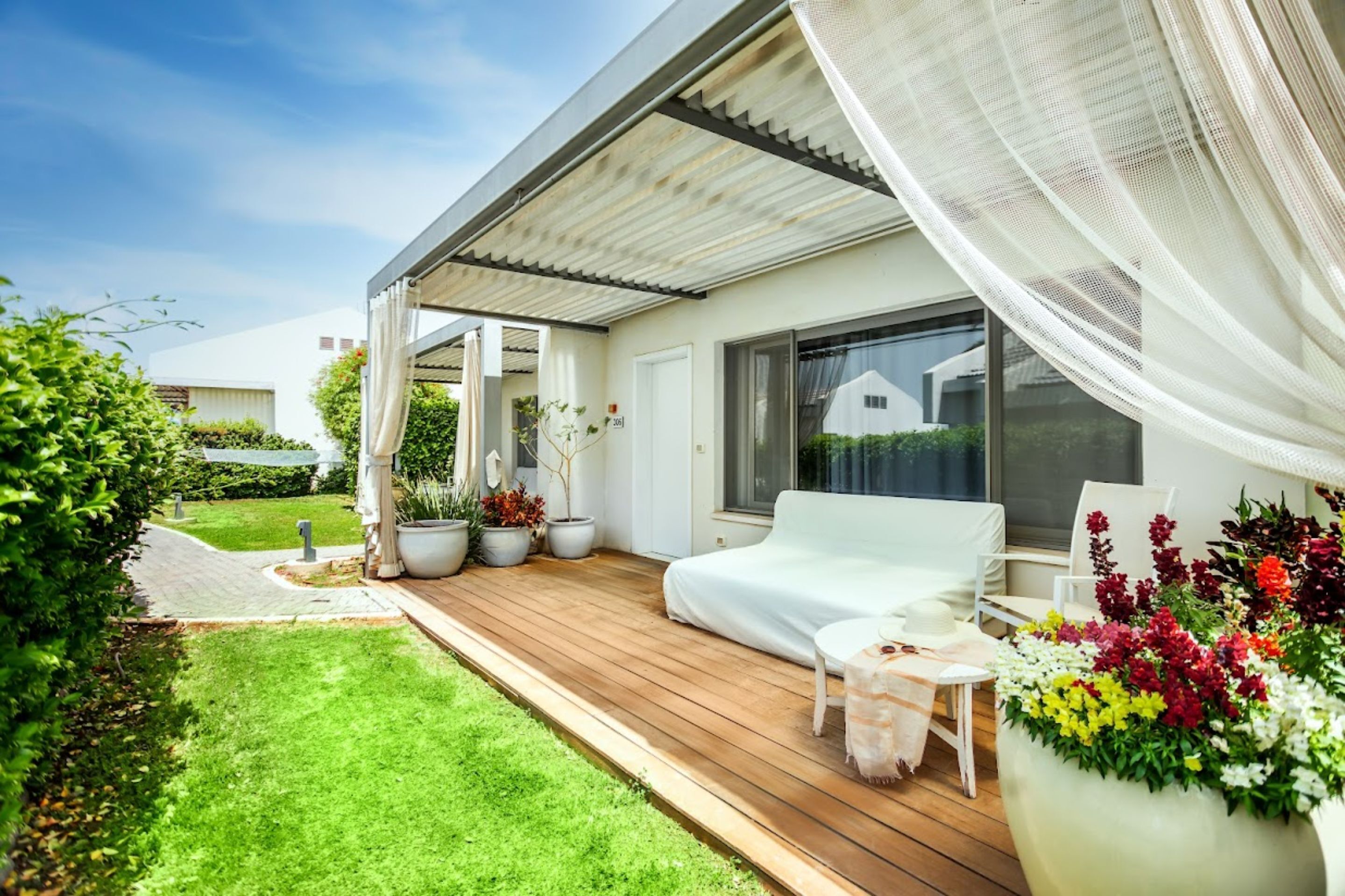 Una casa moderna con terraza de madera, un sofá blanco y una planta grande en maceta.